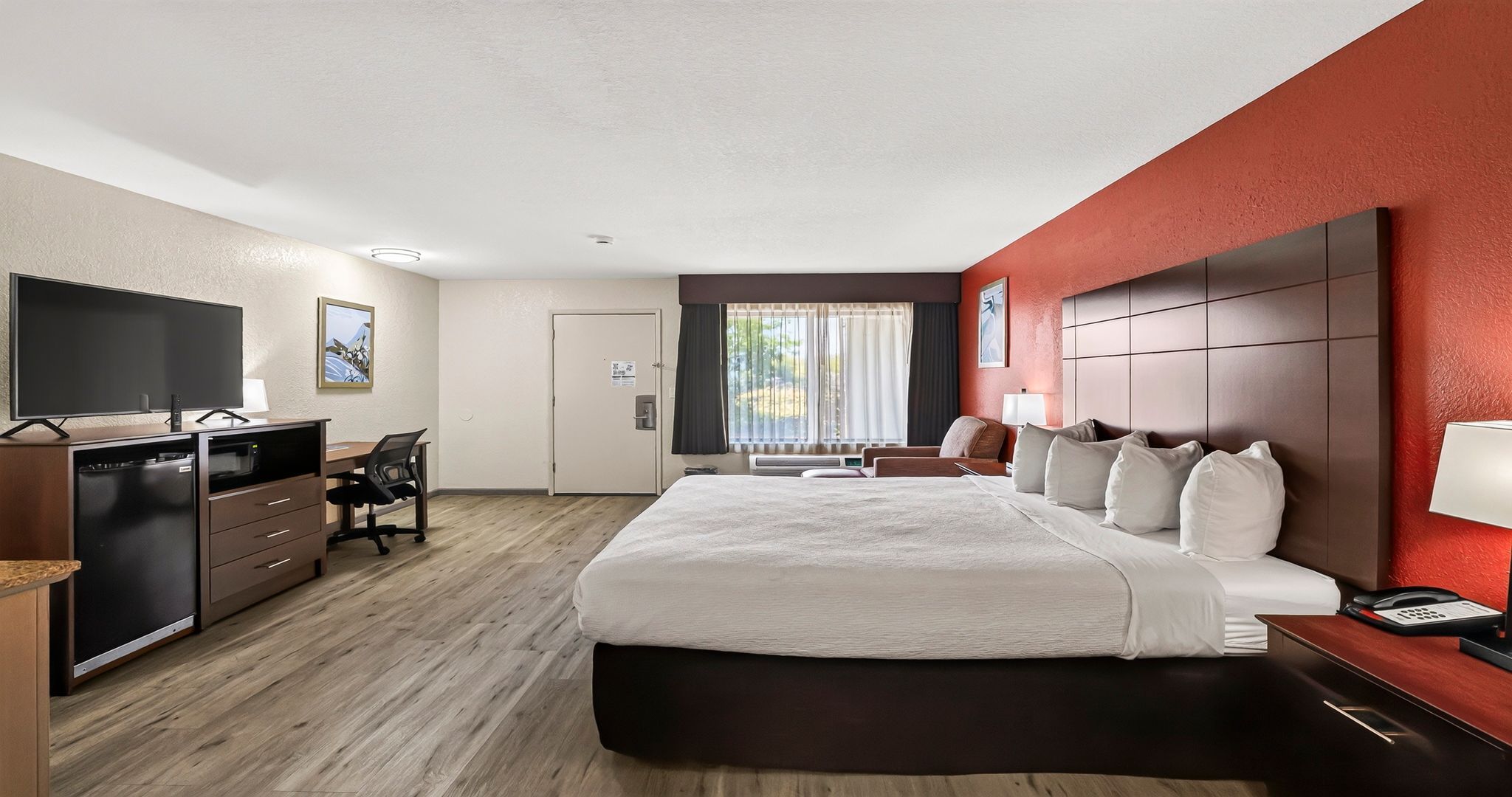 Habitación de hotel con cama, escritorio, televisor y vistas al exterior.