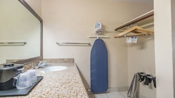 A bathroom with a sink, mirror, towel rack, ironing board, and a shower area.