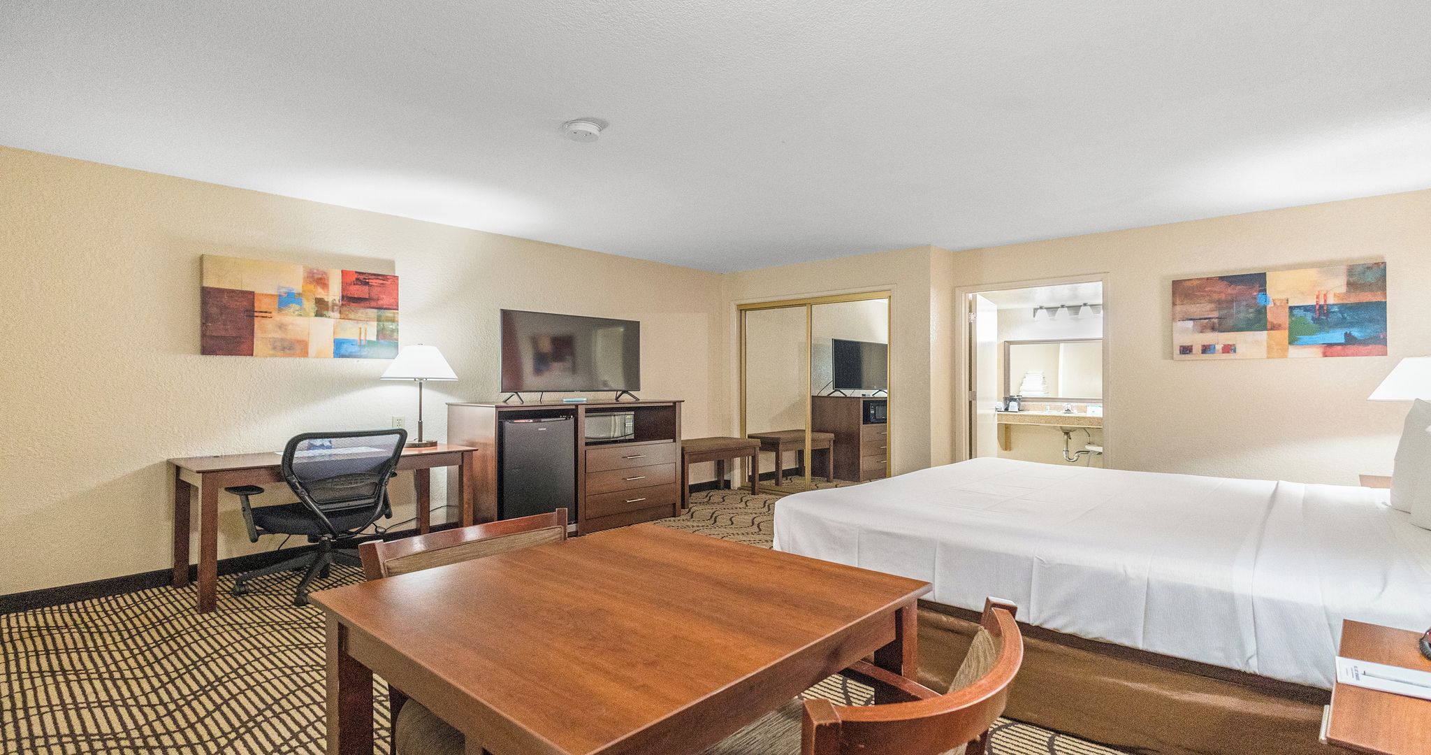 Habitación de hotel con cama, escritorio, silla, televisor y baño con espejo.