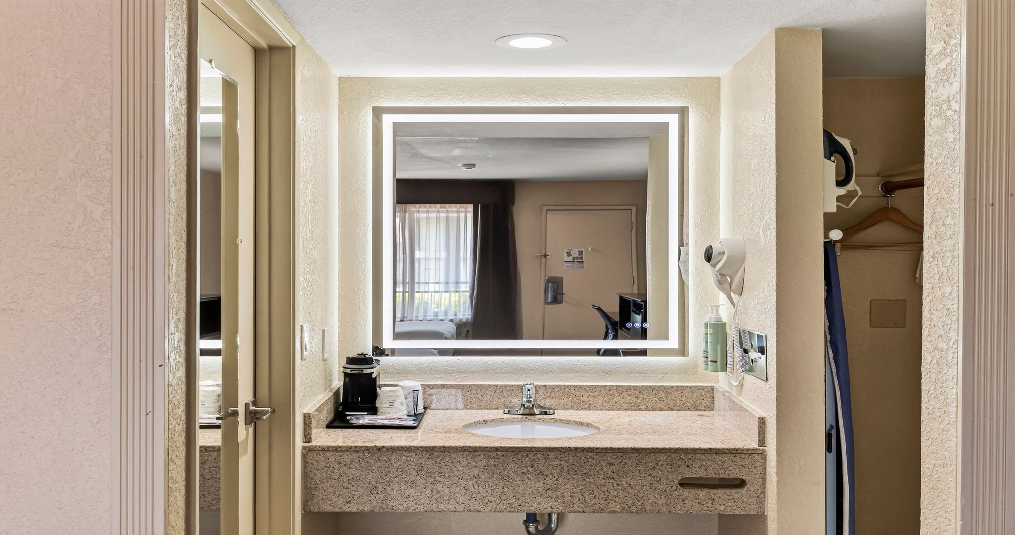 A hotel bathroom with a sink, mirror, and a hairdryer mounted on the wall.