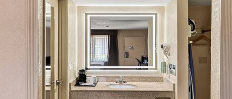 Un baño de hotel con lavamanos, espejo y secador de pelo montado en la pared.