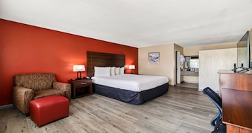 Una camera d'albergo con un letto, una sedia, una scrivania e un bagno visibile attraverso una porta aperta.