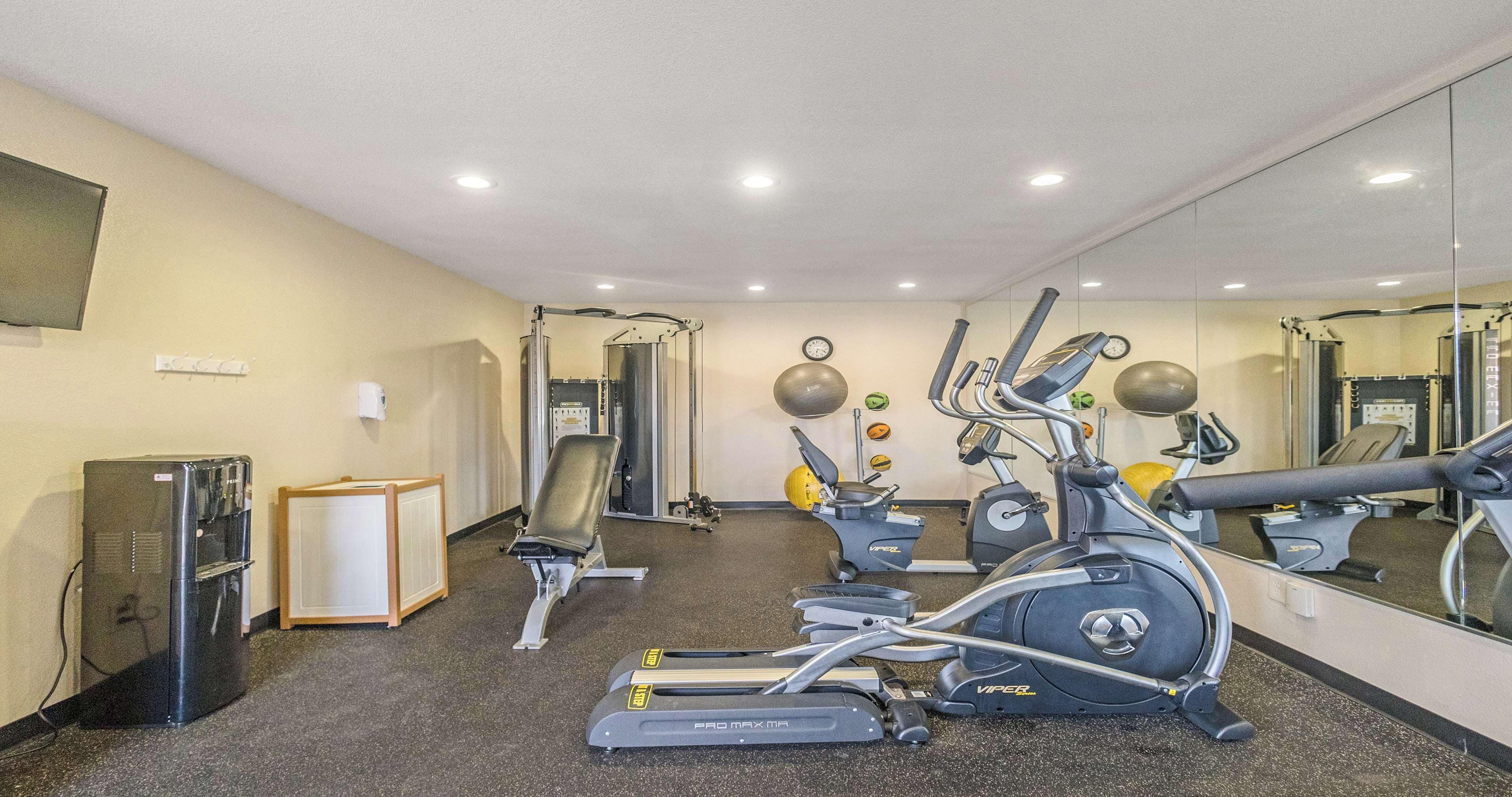 Een fitnessruimte met cardiotoestellen, krachttrainingsapparatuur en een spiegelwand.