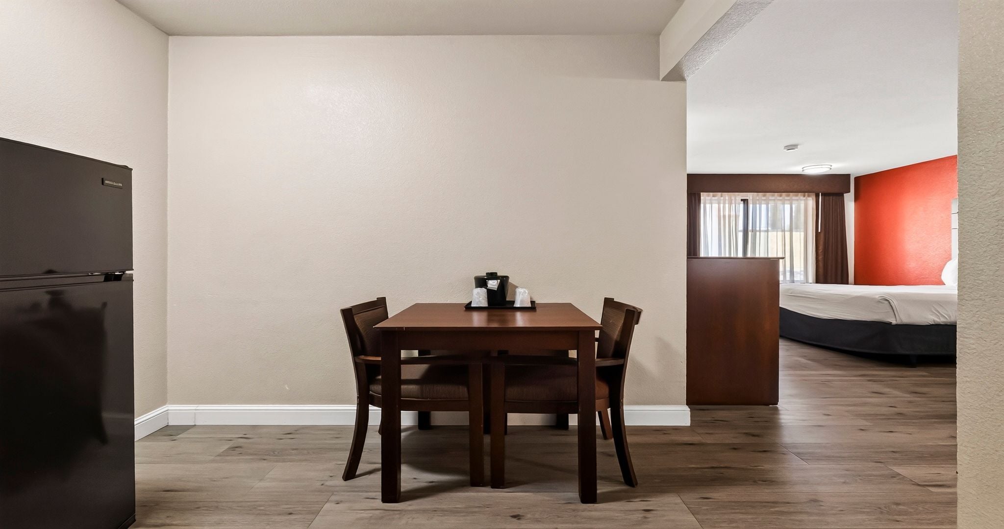 A compact room with a dining table, chairs, a bed, and a kitchenette.