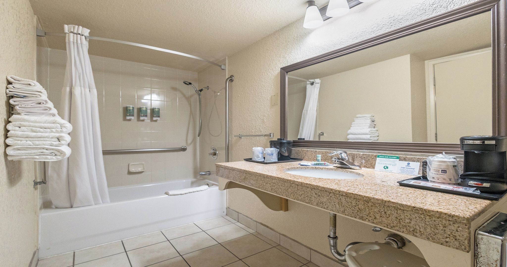 Un baño de hotel con ducha, lavabo, espejo y toallero.