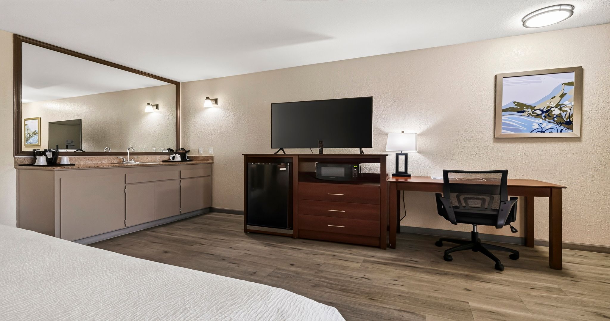 A hotel room with a bed, a desk with a computer, a television, a refrigerator, and a microwave.