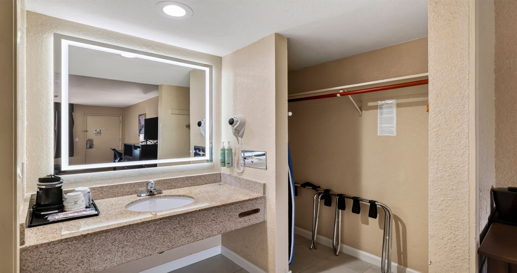 Une salle de bain d’hôtel équipée d’un grand miroir, d’un lavabo, d’un sèche-cheveux et d’un espace douche.