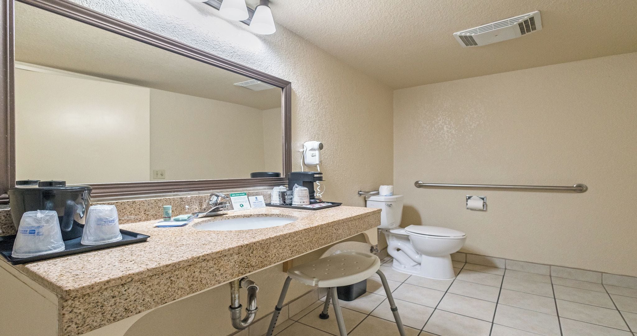 Een hotelbadkamer met een wastafel, spiegel, toilet en een haardroger aan de muur.