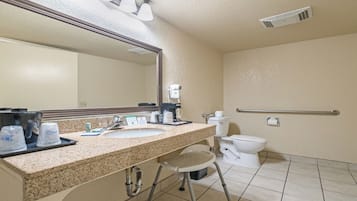 A hotel bathroom with a sink, mirror, toilet, and a hairdryer on the wall.