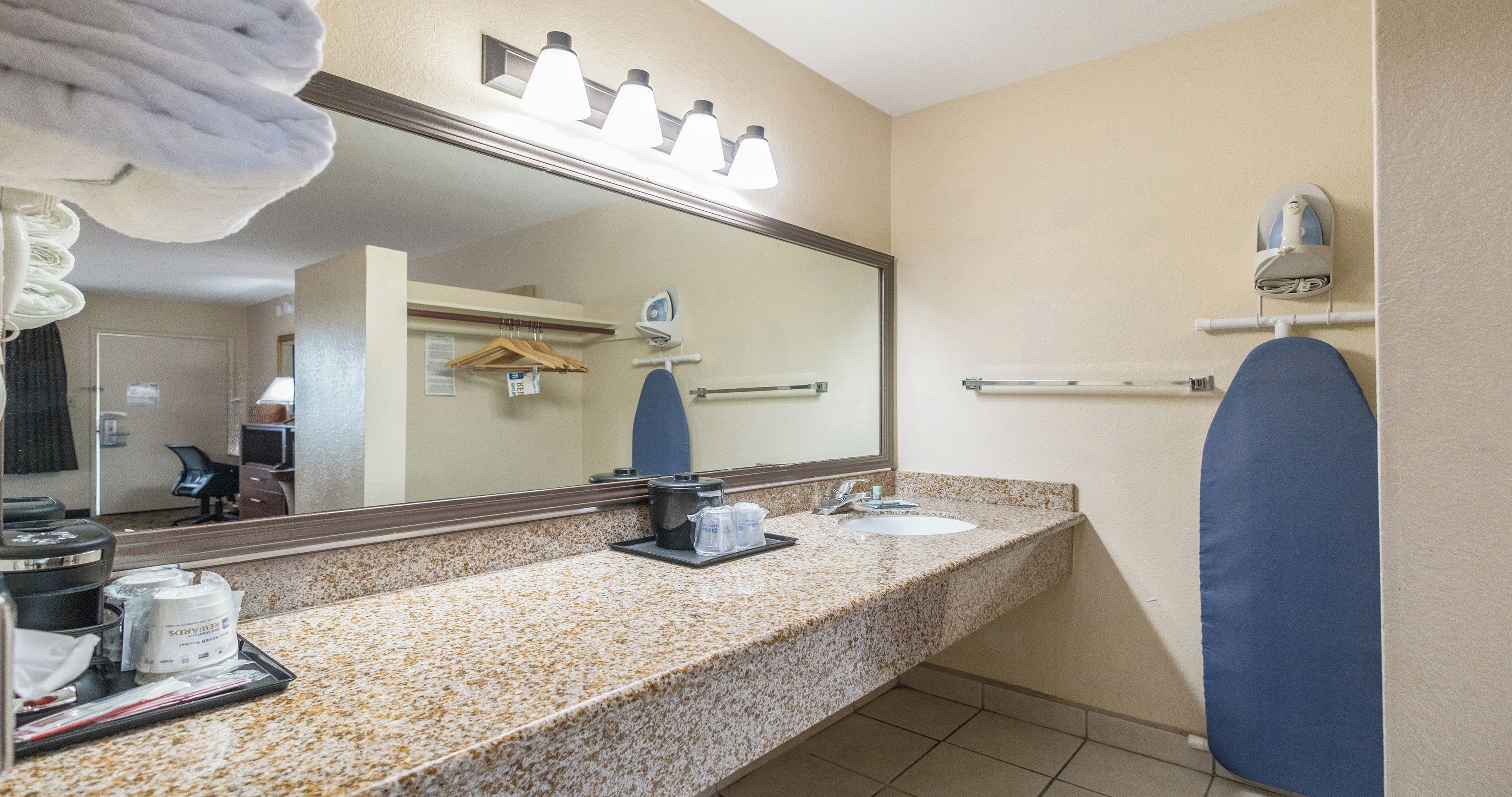 A bathroom with a granite countertop, a sink, a mirror, a towel rack, and a shower area.