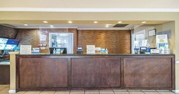 Un mostrador de recepción con detalles de madera, un quiosco digital y señalización informativa.