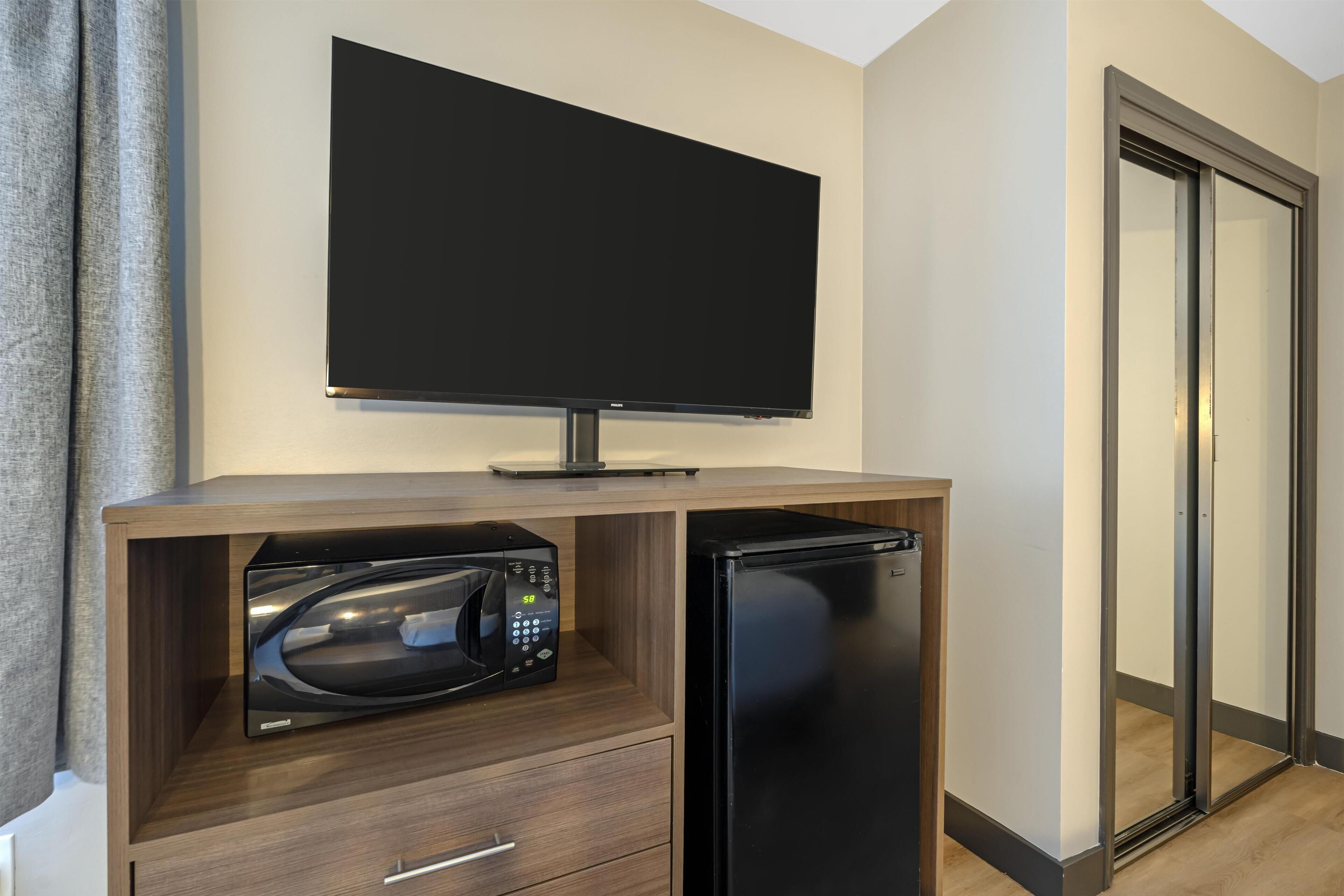 A compact kitchenette with a built-in microwave, a refrigerator, and a flat-screen TV mounted above the counter.