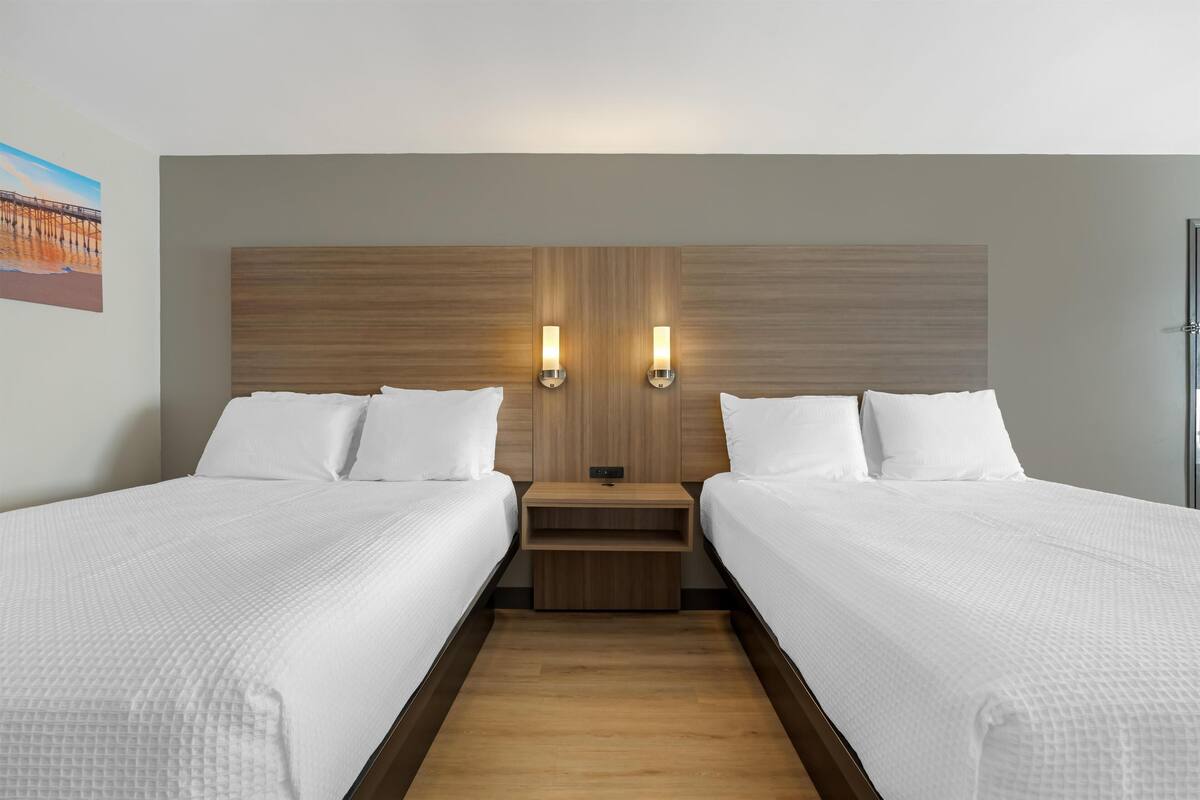 A hotel room with two beds, a wooden headboard, nightstands, and wall-mounted lights.