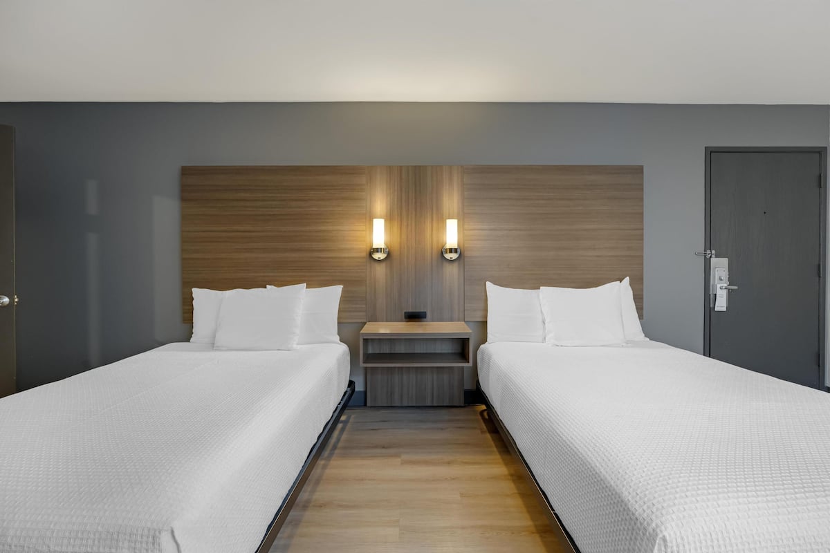 A hotel room with two single beds, a wooden headboard, a nightstand, and two wall-mounted light fixtures.