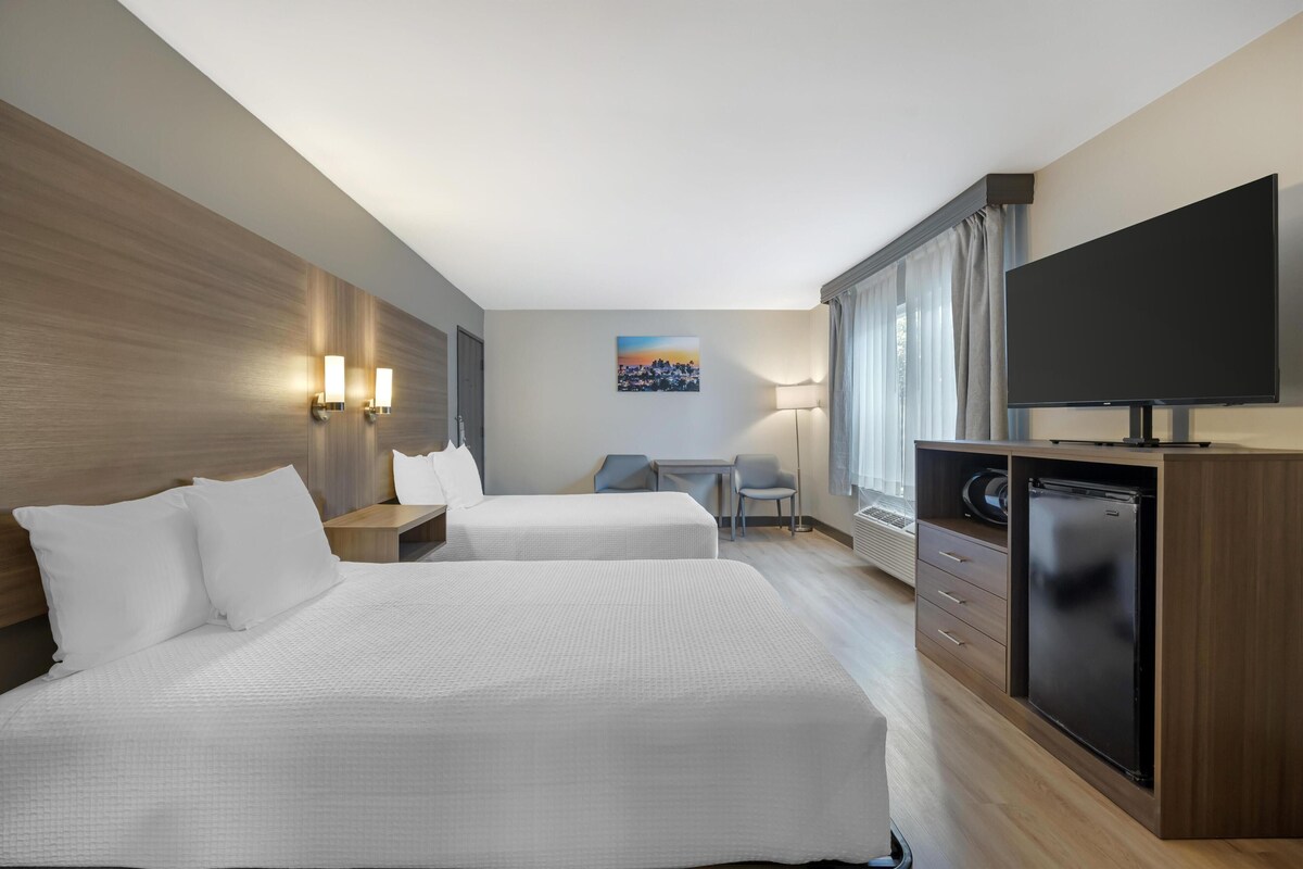 Une chambre d’hôtel avec deux lits, un bureau, une chaise, une télévision et un mini-bar.