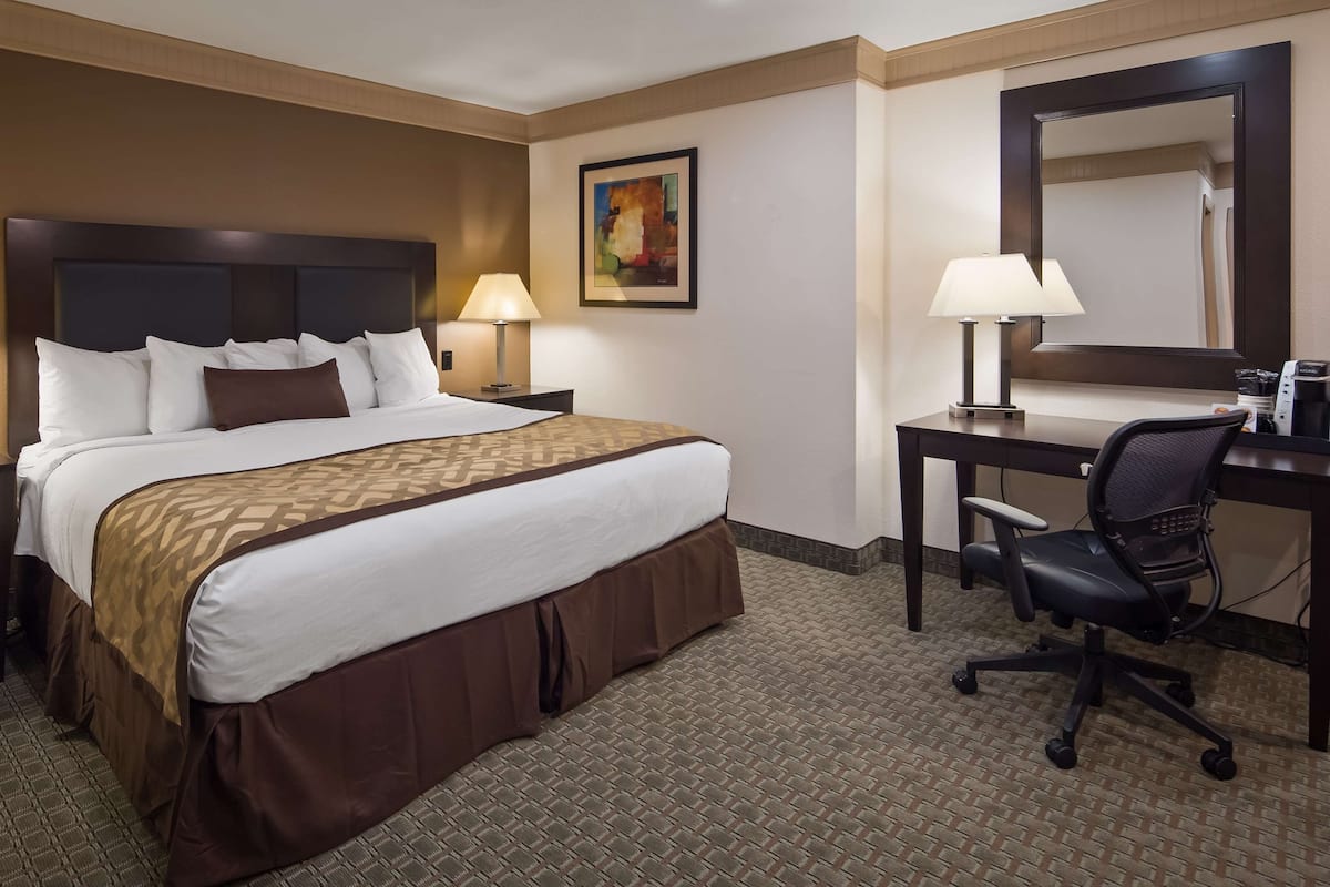 A hotel room with a large bed, two bedside tables with lamps, a desk with a chair, a coffee maker, and a painting on the wall.