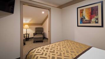 A hotel room with a bed, a chair, a lamp, and a painting on the wall.