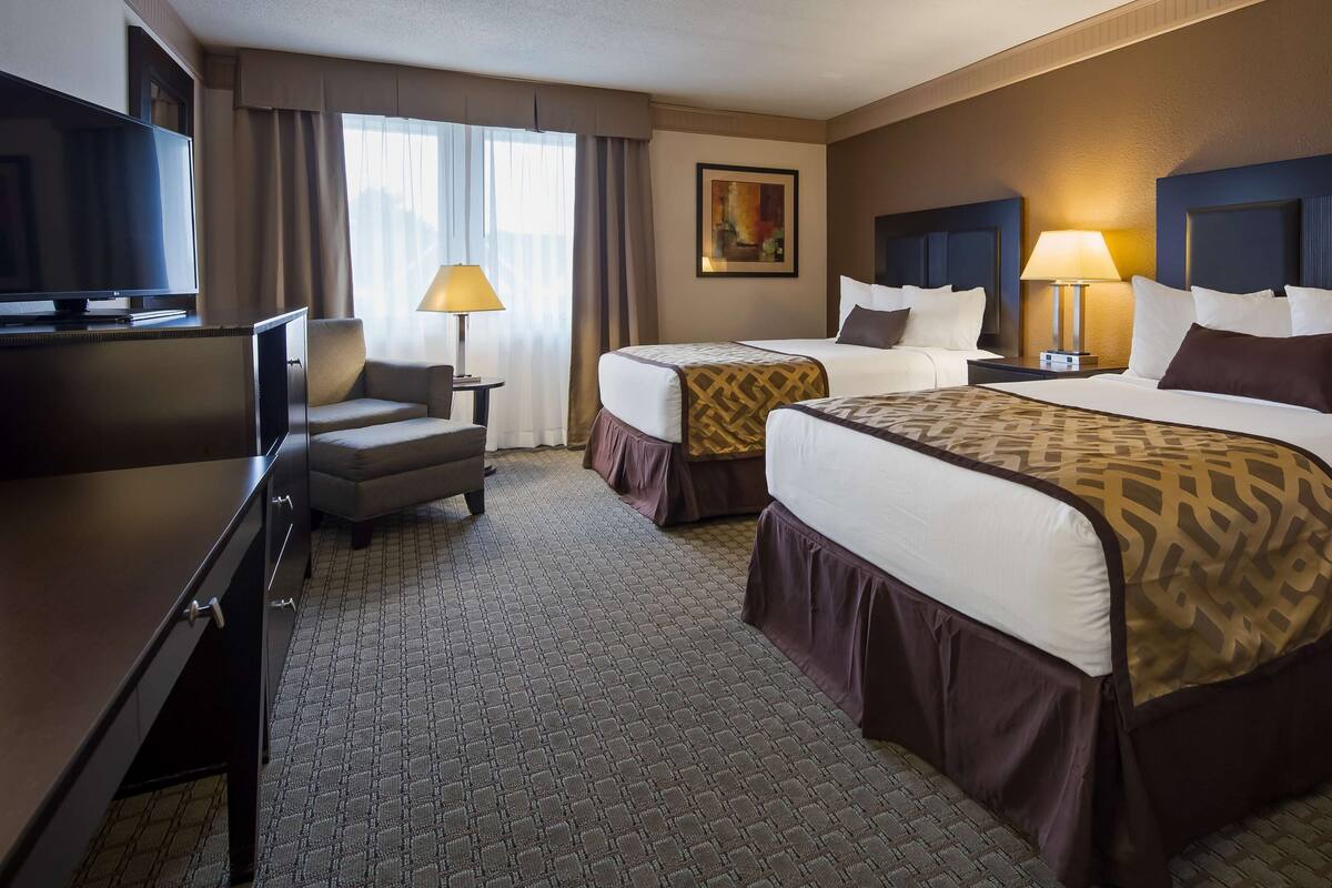 A hotel room with two beds, a desk, a TV, and a lamp.