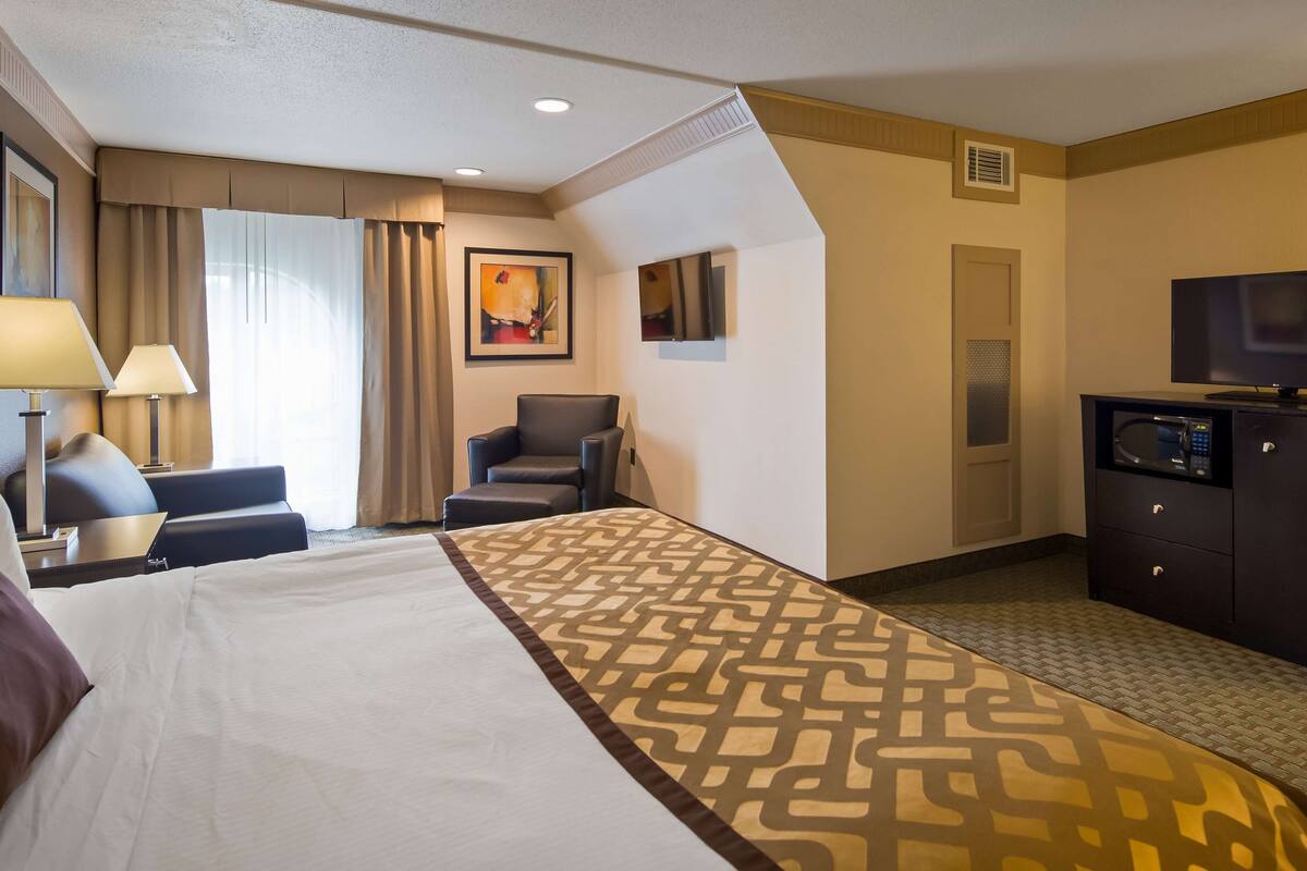 A hotel room with a bed, two chairs, a desk with a lamp, a television, and a minibar.