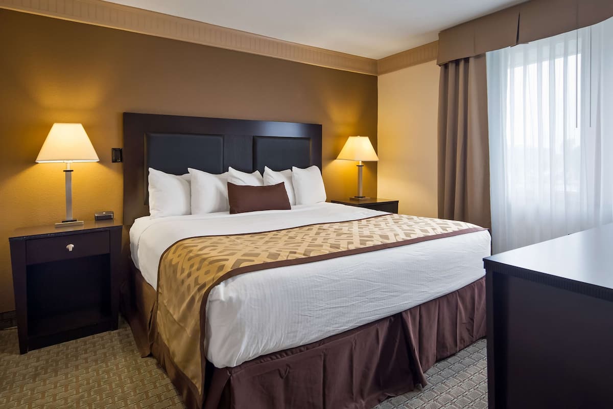 A hotel room with a large bed, two bedside tables with lamps, a desk, and a window with curtains.