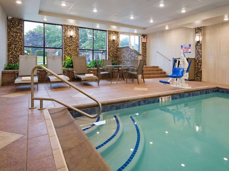 An indoor swimming pool with a lifeguard chair, a pool ladder, and a seating area with chairs and tables.