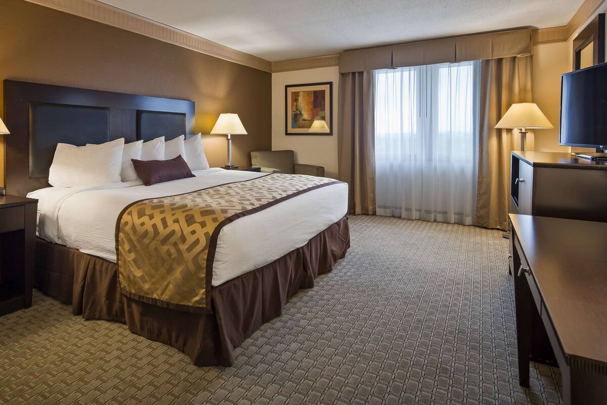A hotel room with a large bed, two bedside tables with lamps, a television, and a large window with curtains.