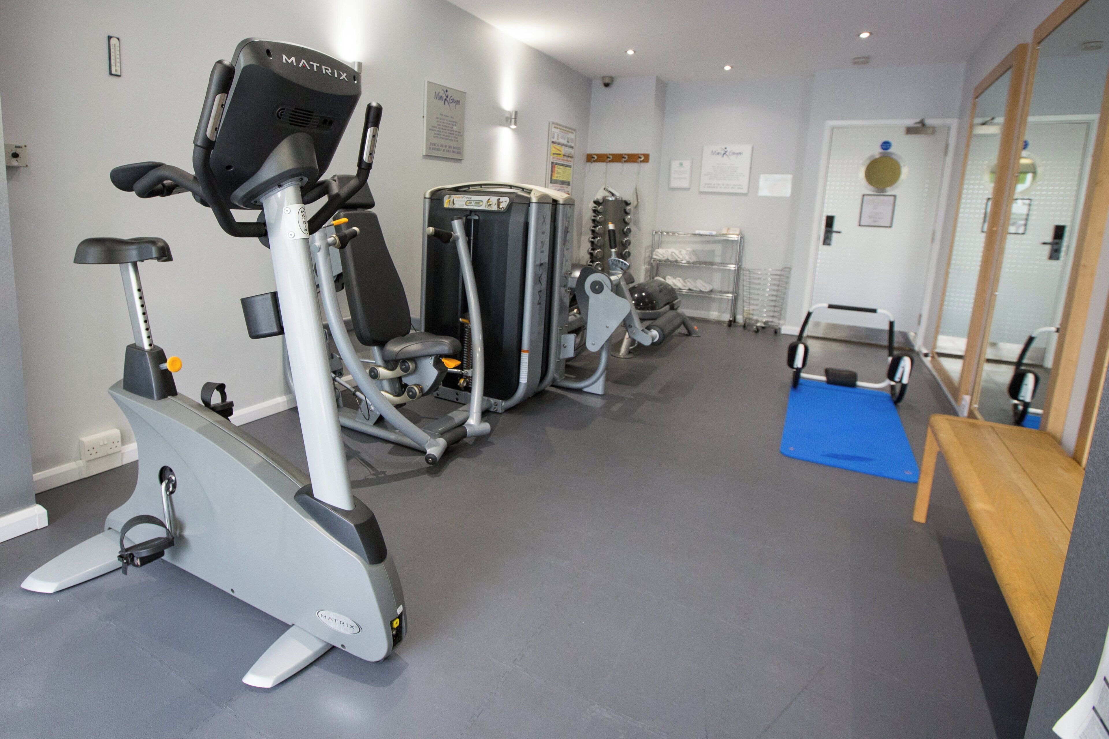 Un gimnasio con máquinas de cardio, equipo de entrenamiento con pesas y un espejo.