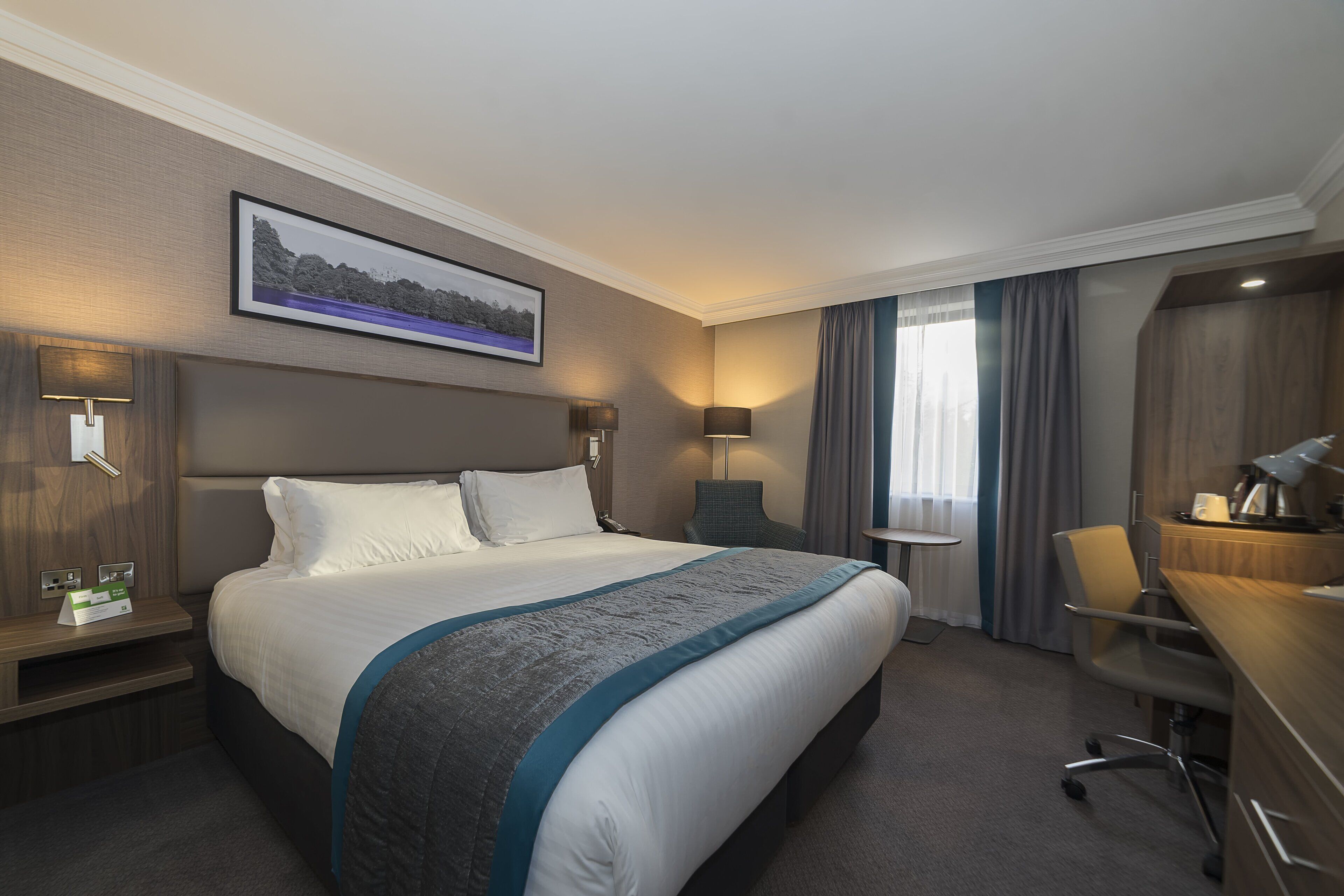 Una habitación de hotel con una cama grande, un escritorio, una silla y vistas al exterior.