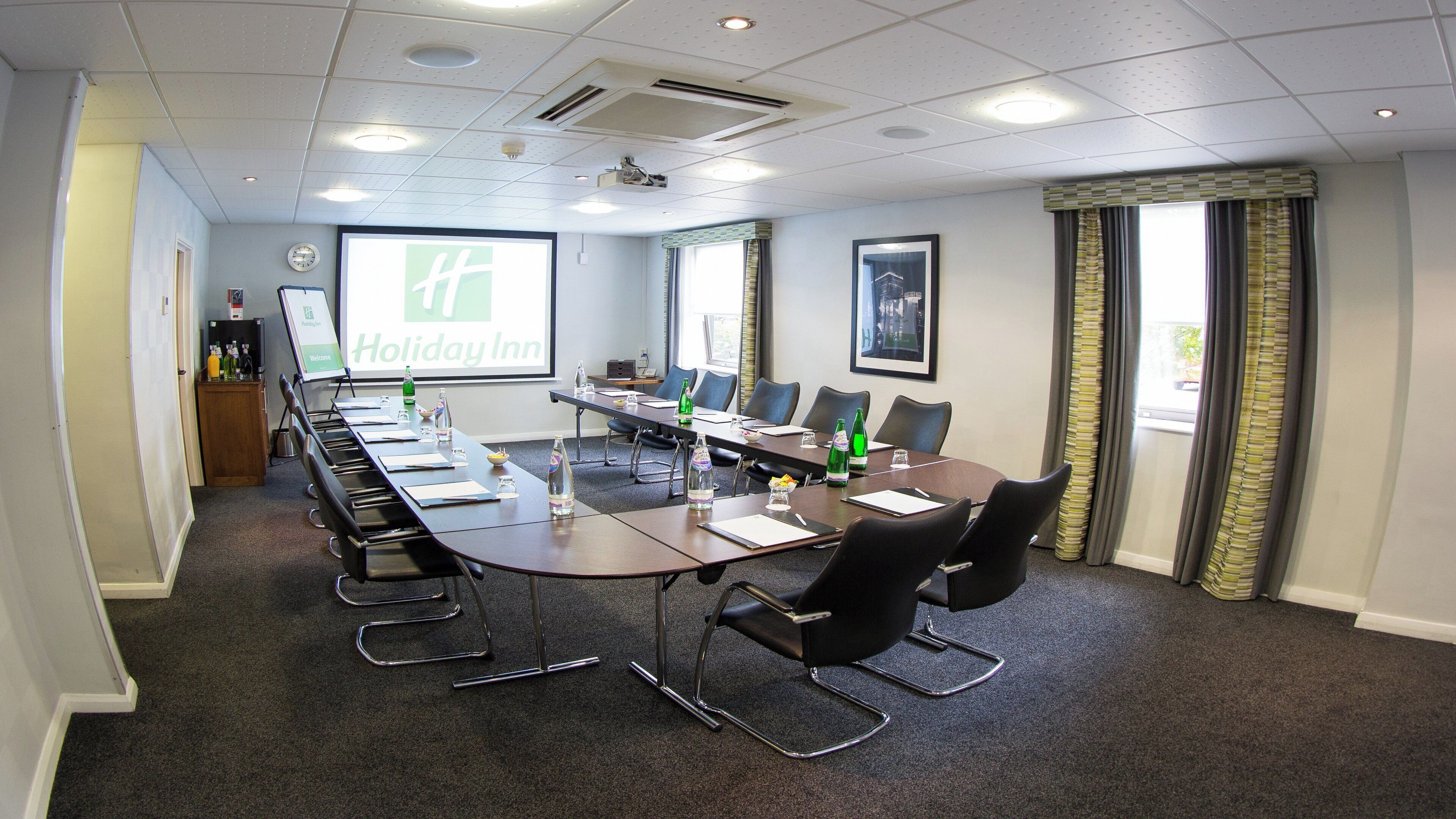 A conference room with a long table, chairs, a projector screen, and a clock on the wall.
