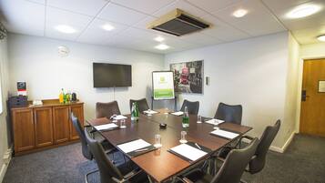 A conference room with a long table, chairs, a television, a clock, and a poster on the wall.