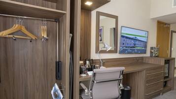 Habitación de hotel con un armario de madera, un escritorio con una silla, un espejo y un televisor mostrando un edificio.