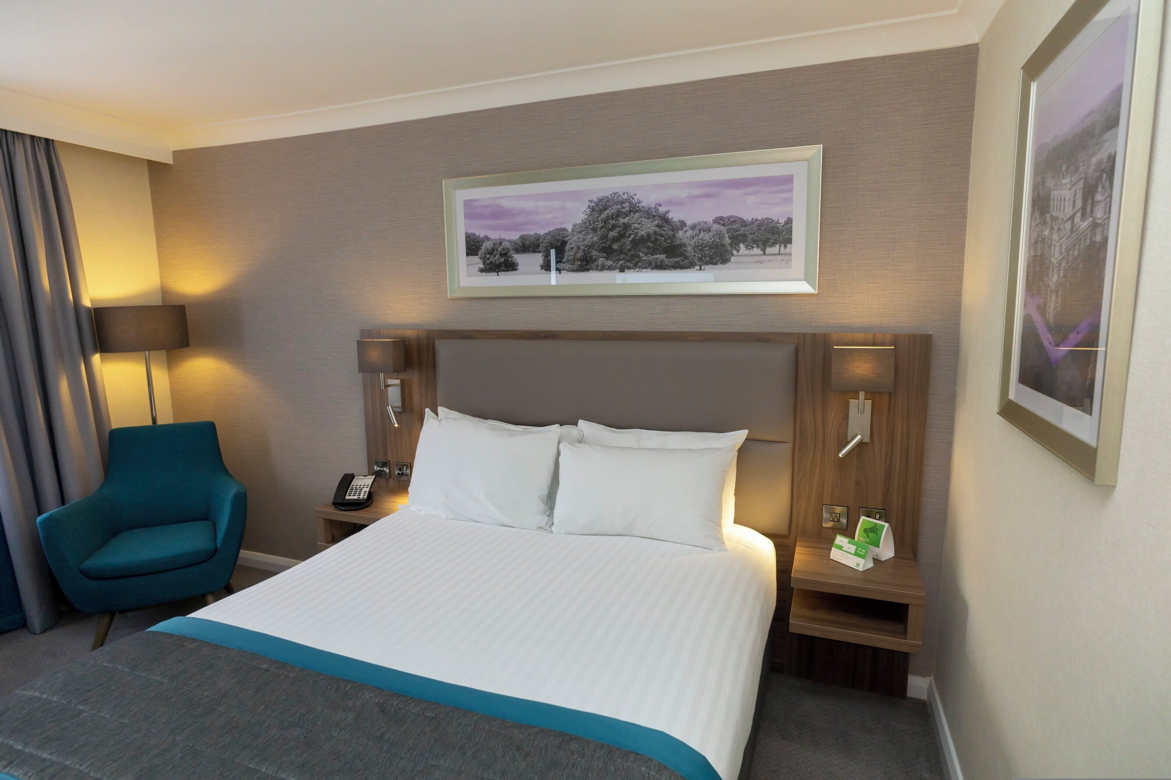 Habitación de hotel con una cama grande, un escritorio, una silla, un teléfono y un cuadro en la pared.