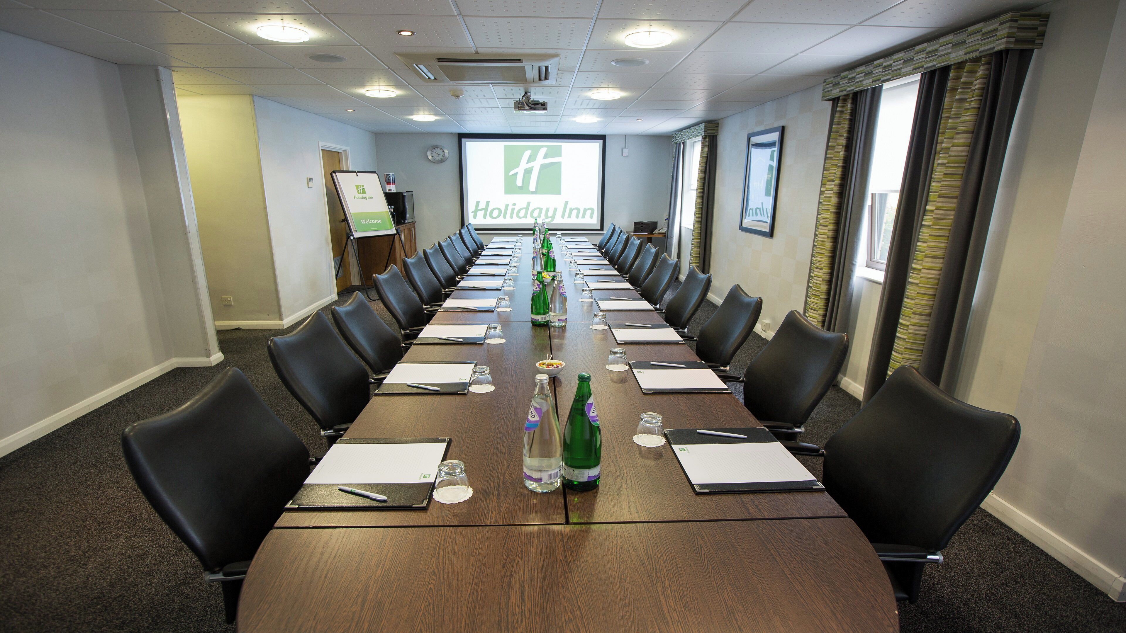 A conference room with a long table, chairs, and a screen displaying the Holiday Inn logo.