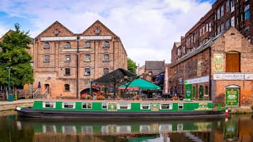 A green boat docked at a canal with a brick building in the background labeled "FELLOWS MORTON CLAYTON HALL".