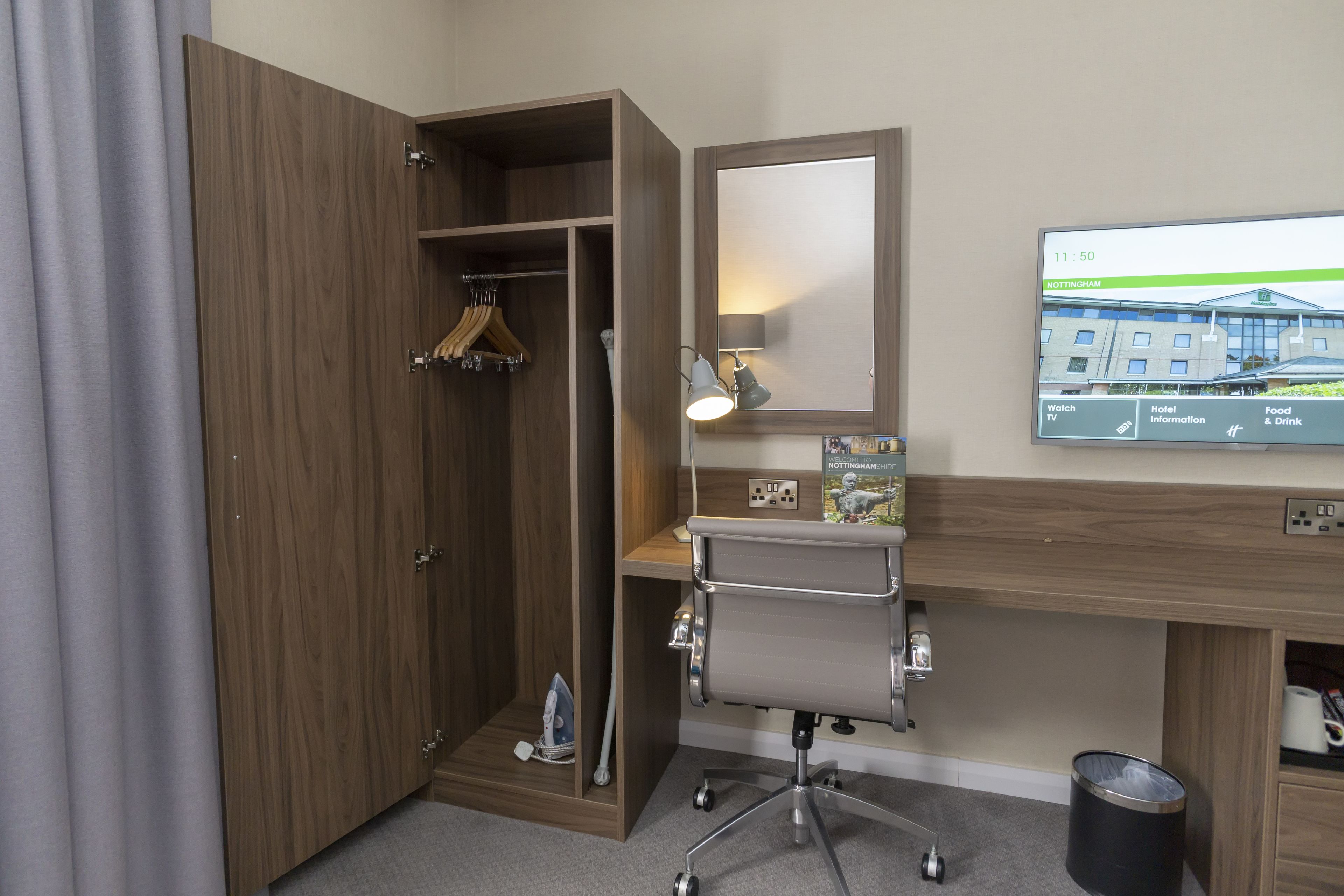 Una habitación de hotel con un armario de madera, un escritorio con silla, un televisor mostrando información del hotel y un espejo.