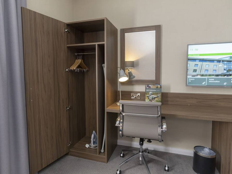 Una habitación de hotel con un armario de madera, un escritorio con silla, un televisor mostrando información del hotel y un espejo.