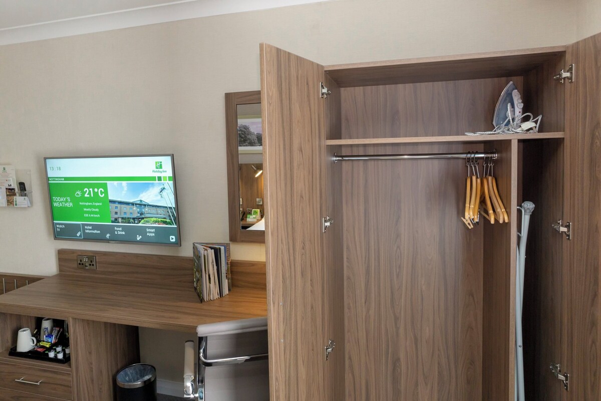 A hotel room with a wooden wardrobe, a television displaying weather information, and a towel rack.