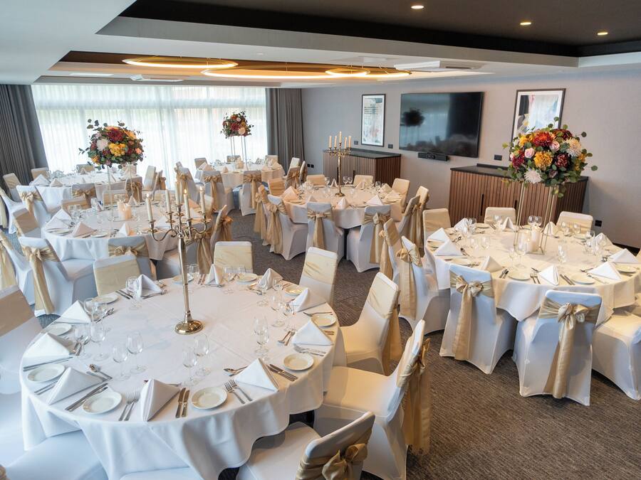 A banquet hall with multiple round tables set for dining, each with white tablecloths and gold sashes.
