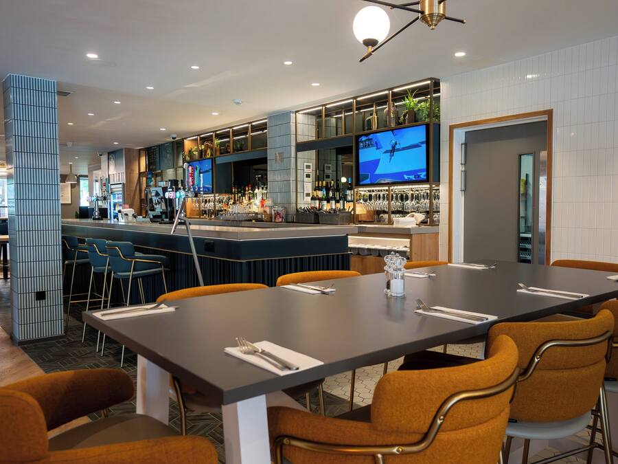 Uma área de bar moderna com um balcão comprido, banquetas e uma tela de televisão.
