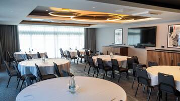 A conference room with multiple round tables, chairs, a large flat-screen TV, and a projector screen.