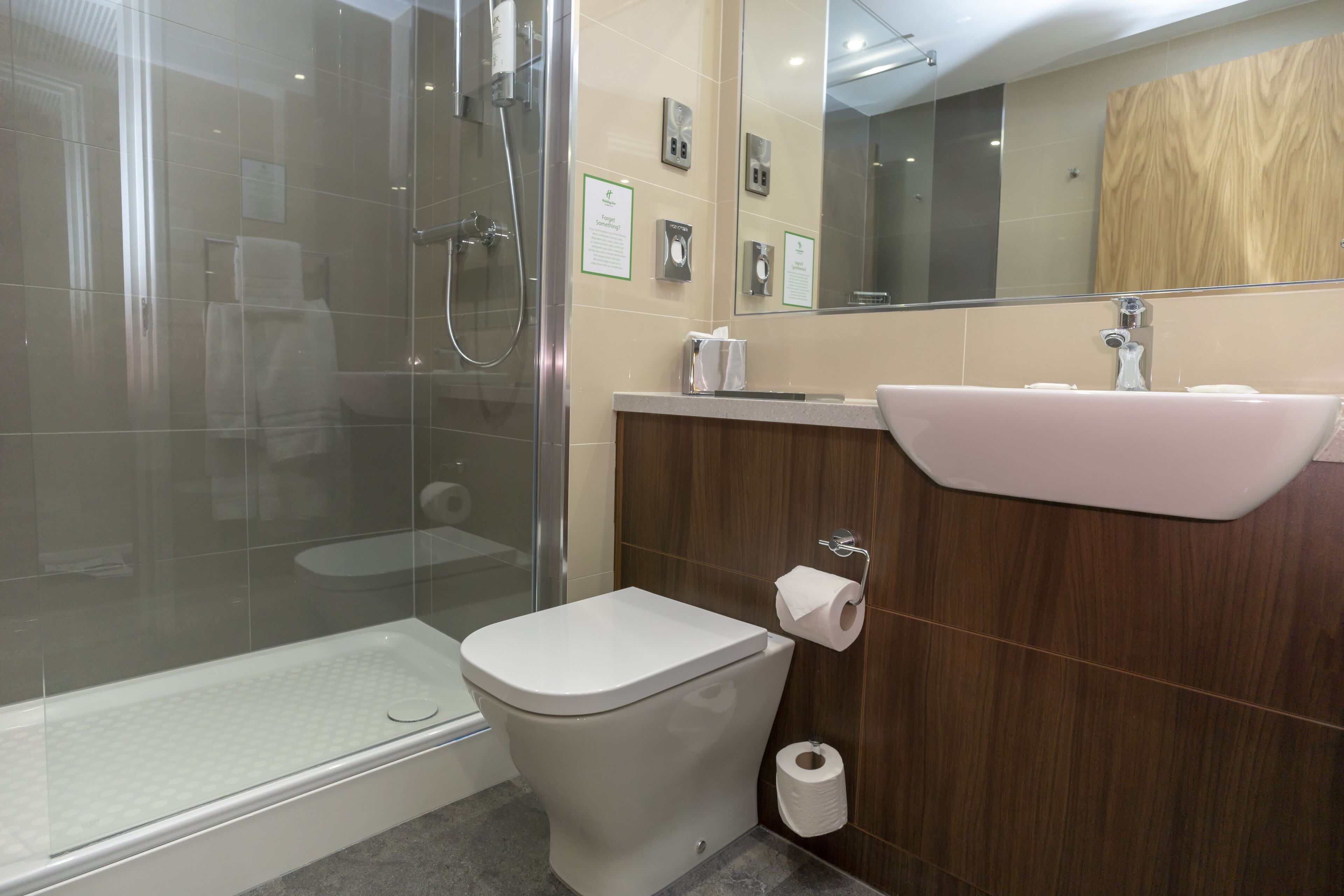 A modern bathroom with a glass-enclosed shower, a white toilet, a sink with a mirror, and a wooden vanity.
