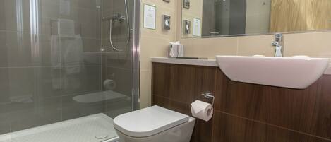 A modern bathroom with a glass-enclosed shower, a white toilet, a sink with a mirror, and a wooden vanity.