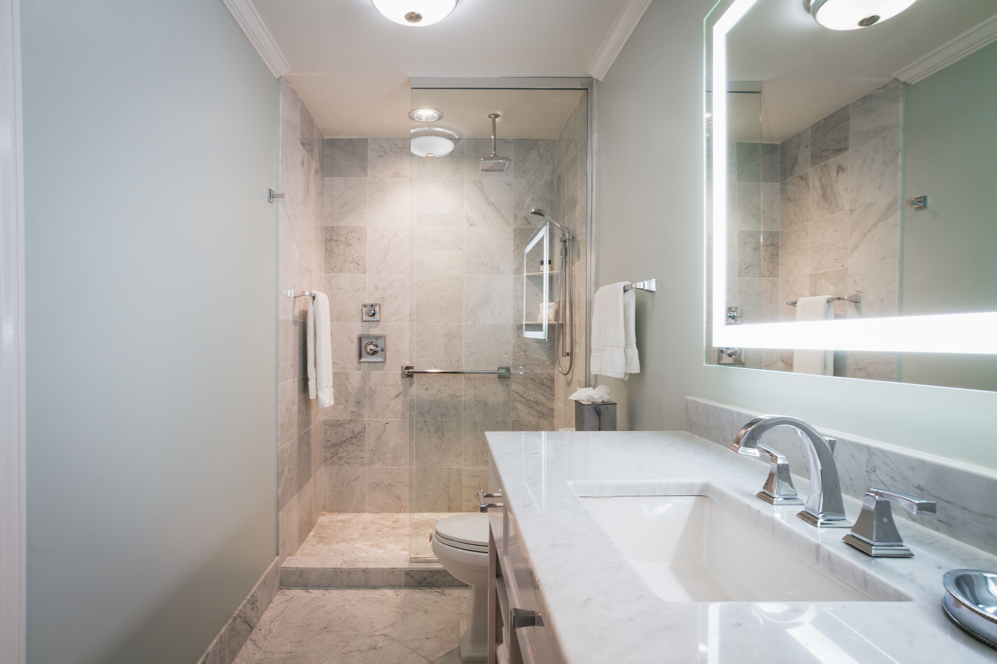 A modern bathroom with a glass-enclosed shower, a large mirror, and a marble countertop.