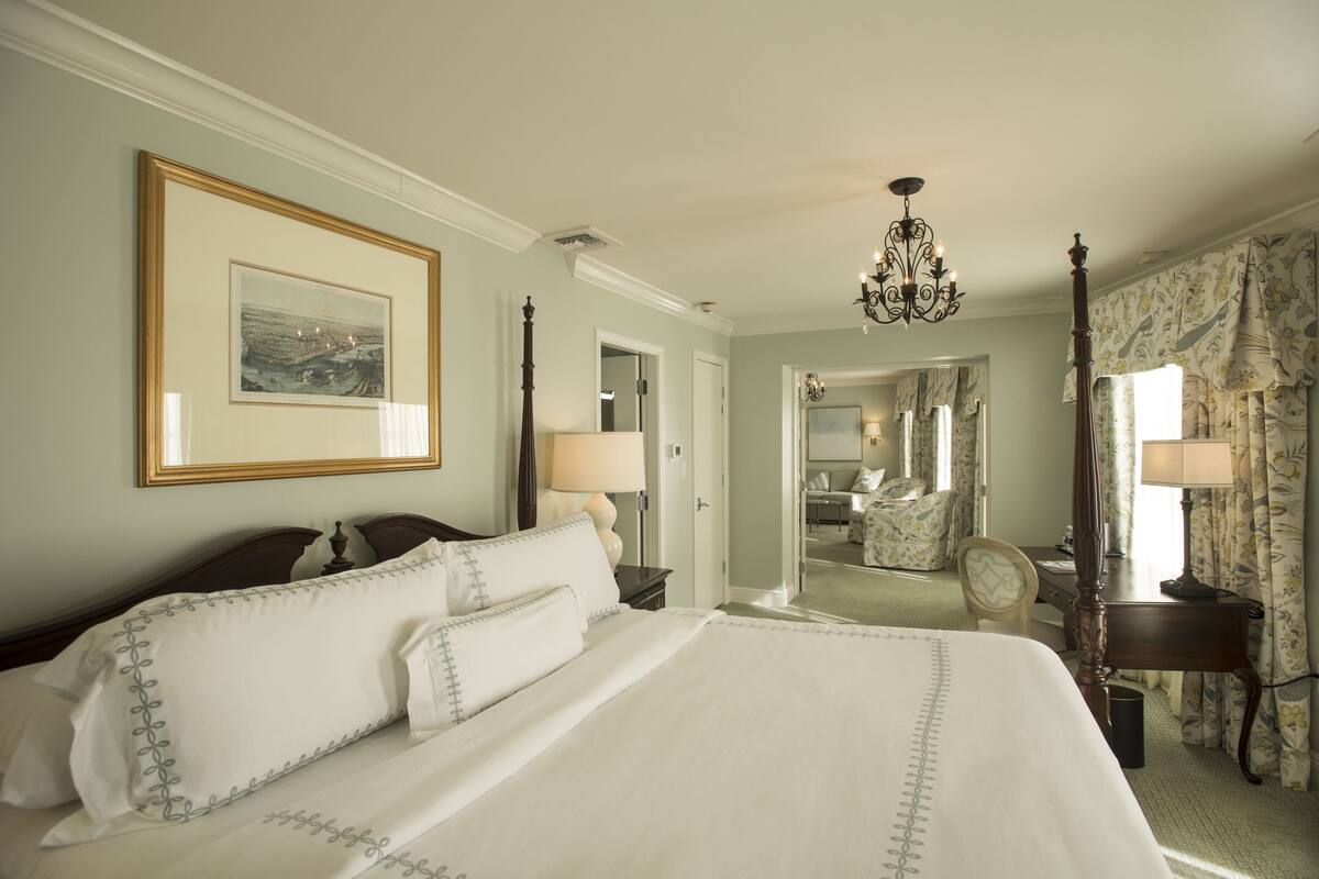 A hotel room with a large bed, a chandelier, a mirror, and a desk with a chair.