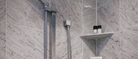 A modern bathroom with a shower, marble tiles, and built-in shelves with toiletries.