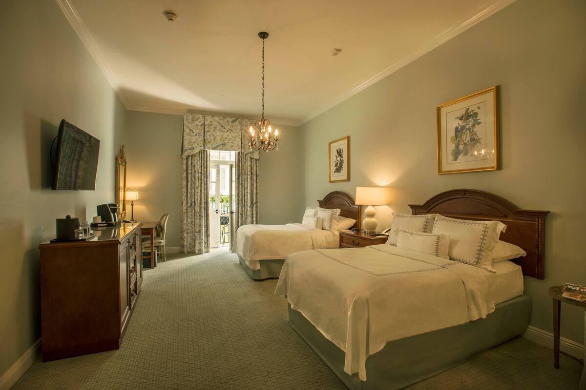 A hotel room with two beds, a desk with a lamp, a dresser, and a chandelier.