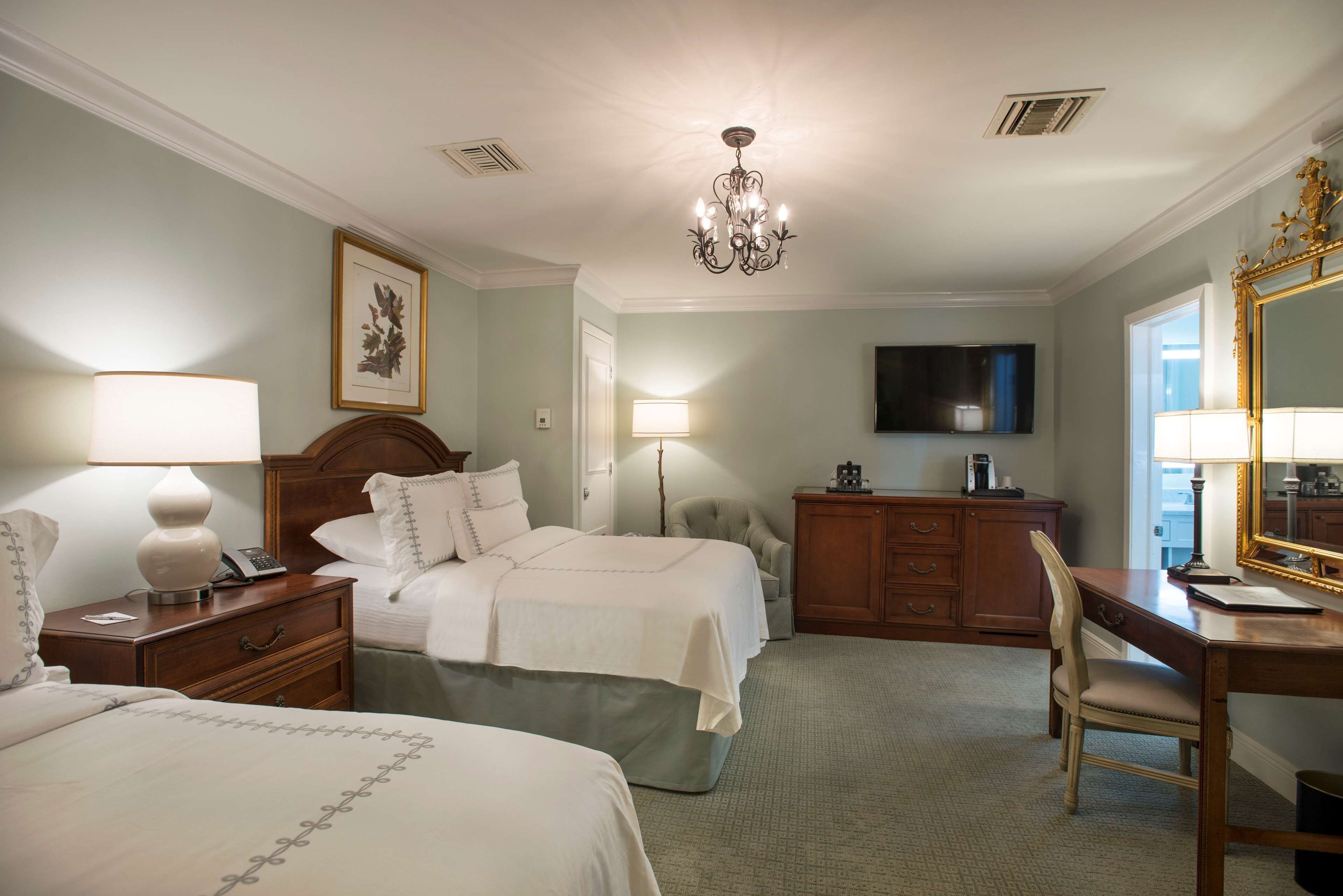 Een hotelkamer met twee bedden, een bureau, een stoel, een televisie en een kroonluchter.