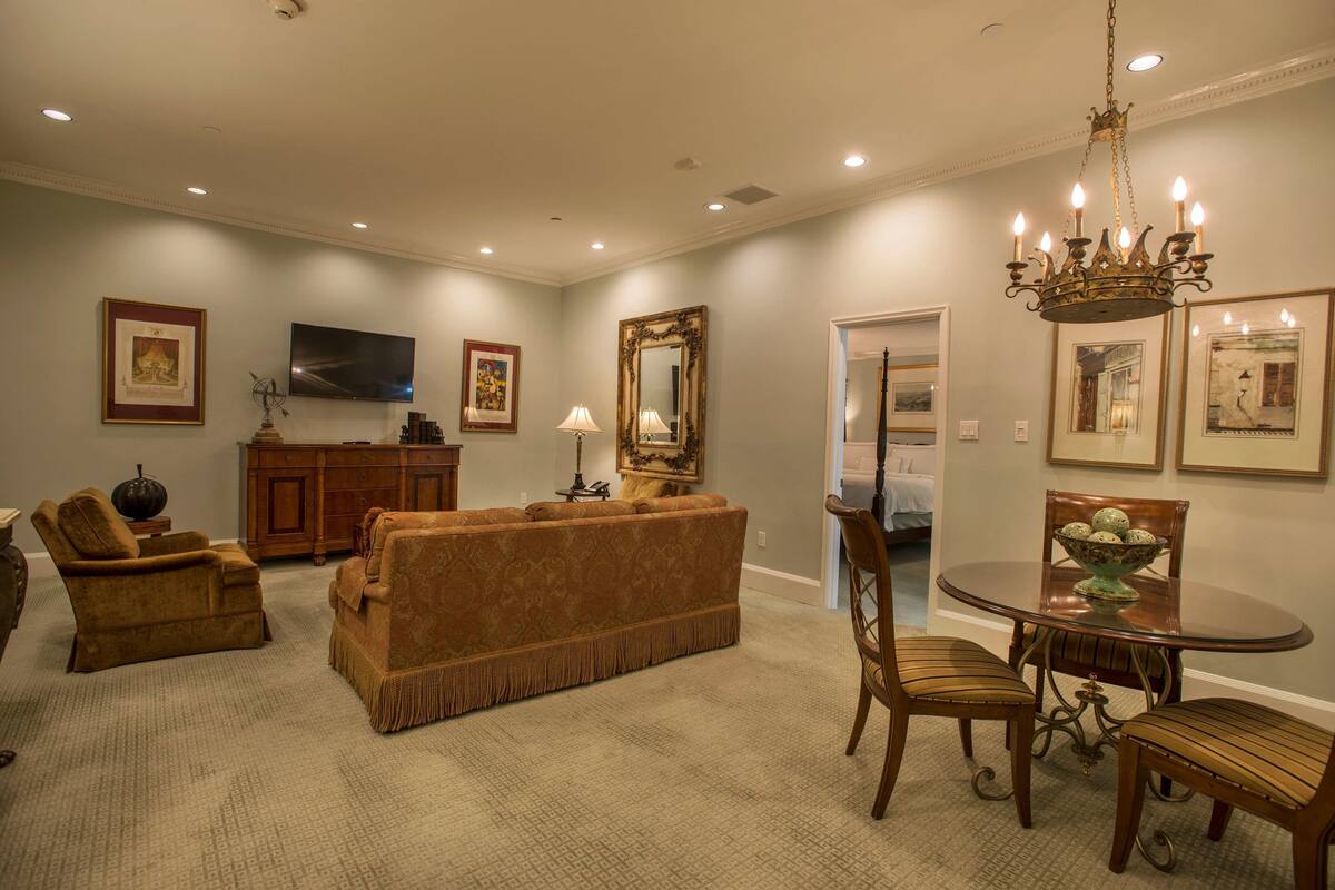 A living room with a brown sofa, a wooden dining table with chairs, a chandelier, and framed artwork on the walls.