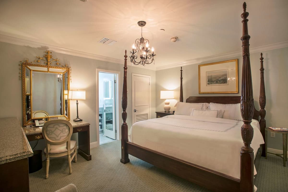 A four-poster bed with a chandelier, a large mirror, and a desk with a chair.