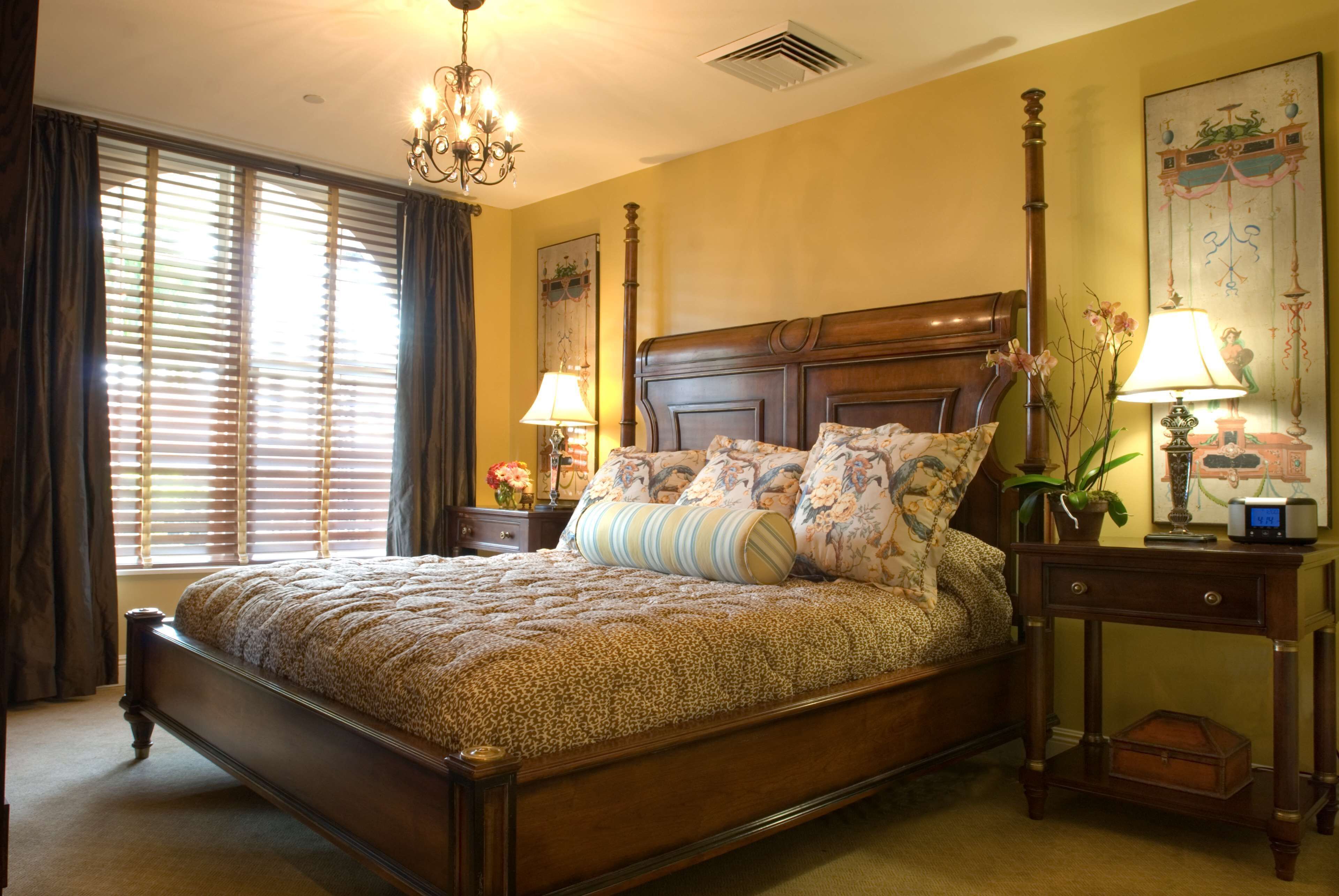 A large bed with a wooden headboard, two bedside tables with lamps, and a window with blinds.
